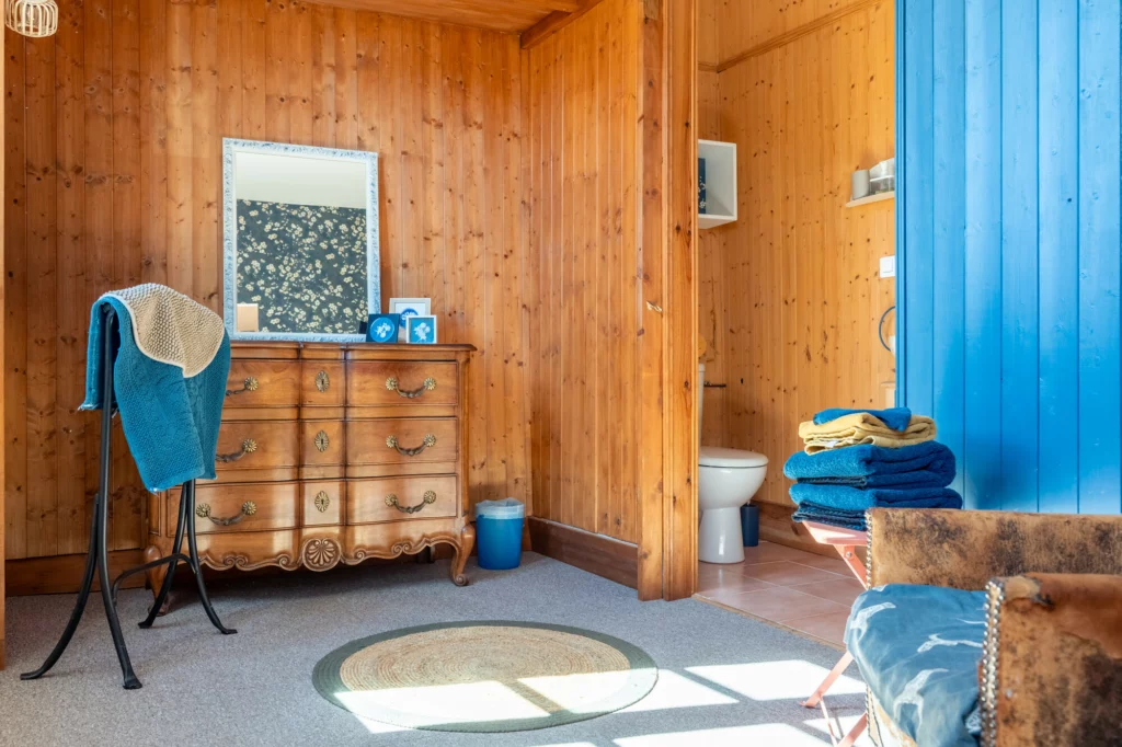 Chambre Florale à Casa Bella : commode en bois, serviettes bleues et tapis rond, murs lambrisés, à Charroux